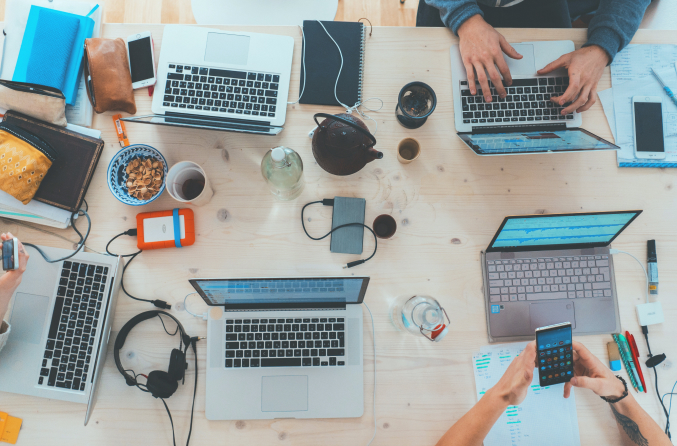 Communal work desk showing five laptops, phones and leads